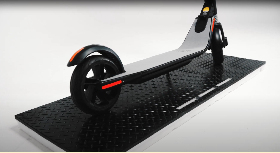 An e-scooter parked on a Meredot wireless charging mat, demonstrating cordless charging.