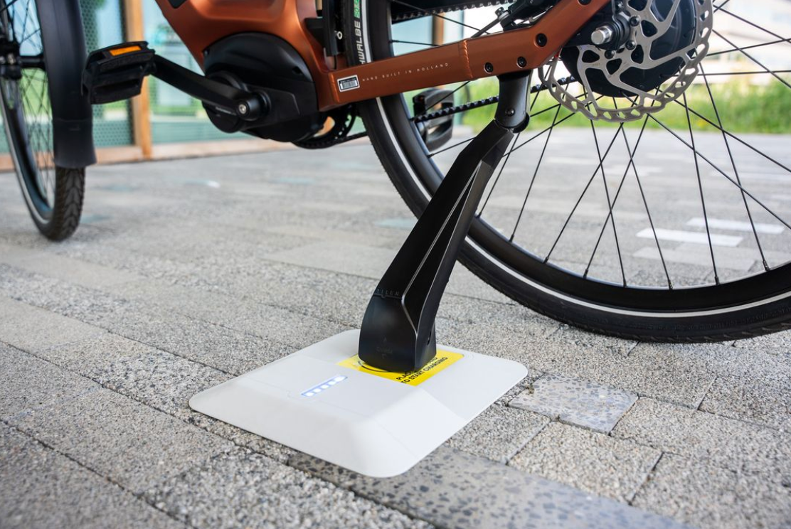 Tier wireless charging pad embedded in pavement with an e-bike kickstand resting on it