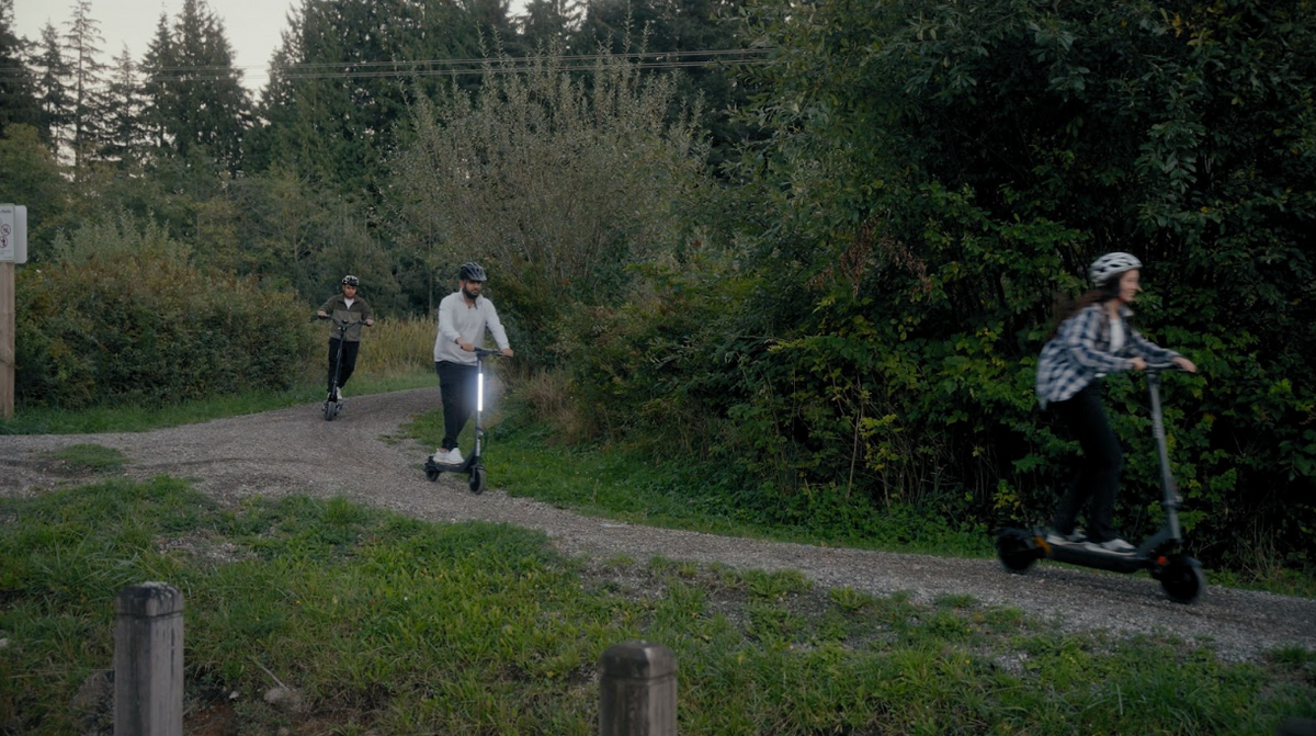 Three adults riding e-scooters on a path in the woods