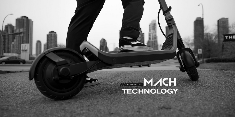 Person riding an electric scooter on a city street with Mach Technology branding.